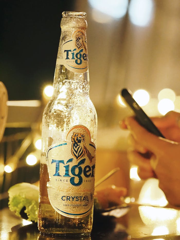 services-03 A bottle of Tiger beer on a table with a smartphone in a Hồ Chí Minh bar, capturing a vibrant night scene.