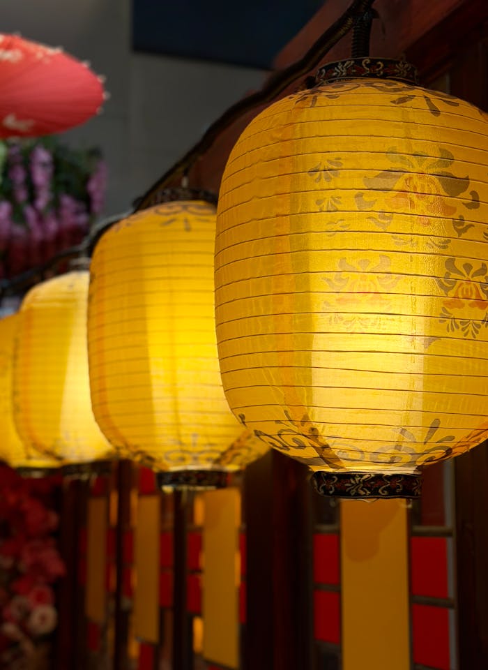 our-experience Row of glowing yellow paper lanterns in a vibrant market setting at night.